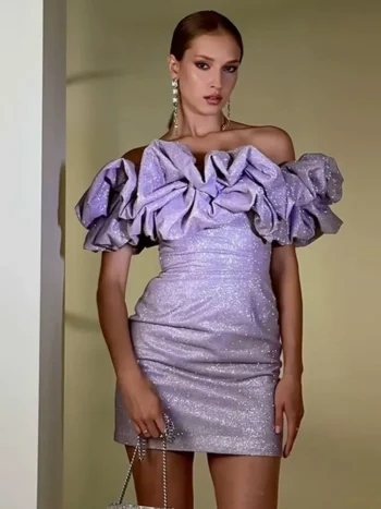 A woman wearing a glamorous off-the-shoulder lilac mini dress with oversized ruffle sleeves, posing elegantly indoors.