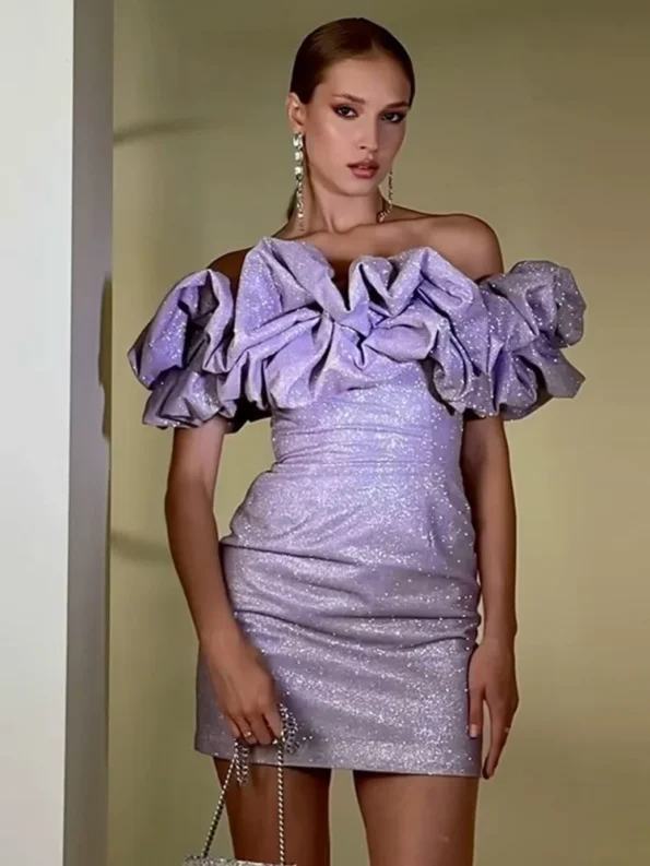 A woman wearing a glamorous off-the-shoulder lilac mini dress with oversized ruffle sleeves, posing elegantly indoors.