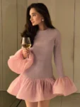 Woman wearing long sleeve knit mini dress with puffy hem and flare cuffs