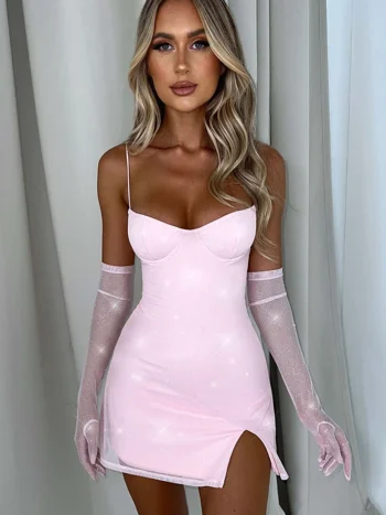 A woman wearing a glamorous light pink spaghetti strap mini dress with a thigh slit, paired with sheer matching gloves, posing elegantly indoors.
